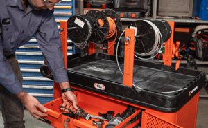 Male electrician using the RAILWORKS industrial utility cart outfitted with the mesh single door security panel, wire spool holders, and tool drawer in an industrial MRO setting