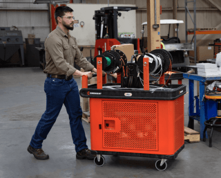 Male technician pushing a RAILWORKS industrial cart with wire spool holders mounted on top and a mesh security wrap through a warehouse