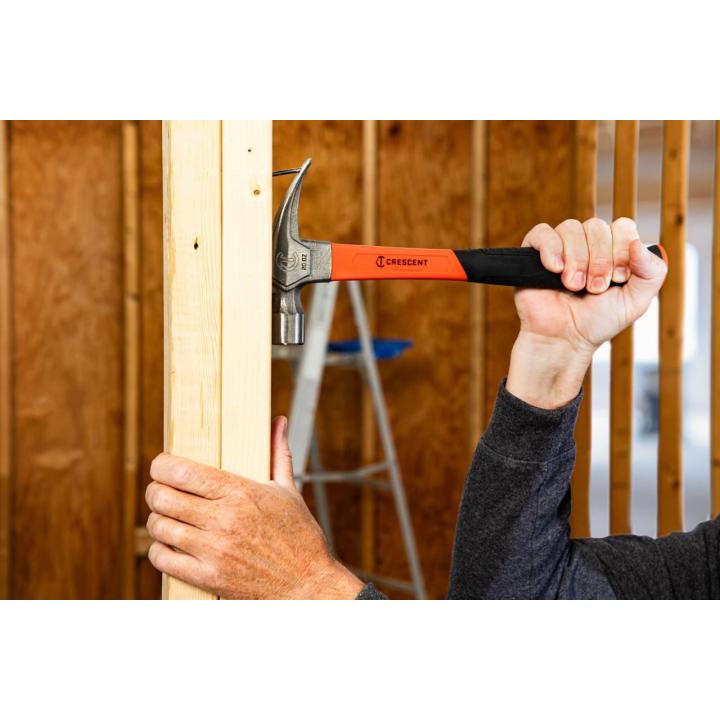 Worker holds a wood stud while raising a Crescent 20 oz. claw hammer to drive a nail in unfinished wall framing.