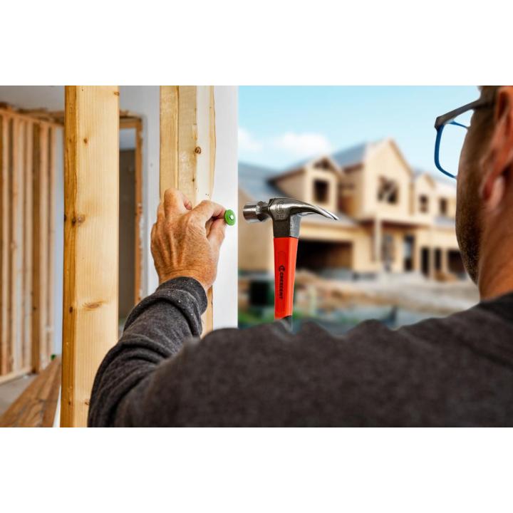 Worker holds a green nail against a wall stud while positioning a Crescent 16 oz. claw hammer in an unfinished house.