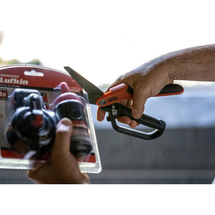 Hand using orange and black shears to cut plastic packaging.