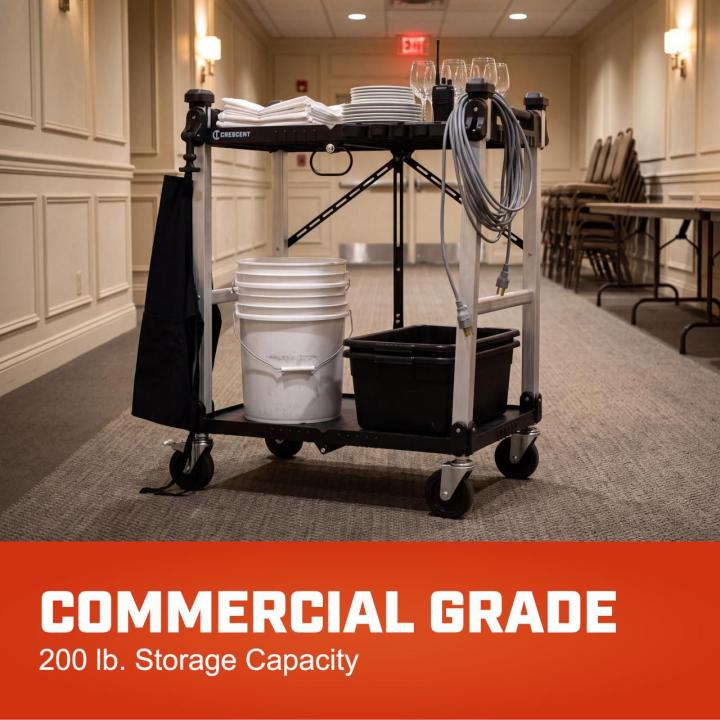 Two-shelf utility cart on casters holds linens, dishes, glasses and utility buckets.  Banner reads COMMERCIAL GRADE  for 200 lb. Storage Capacity.