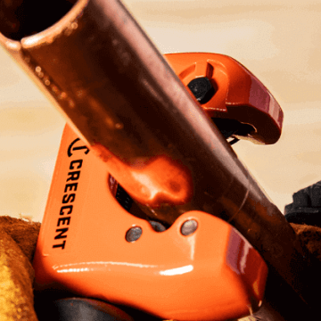 Male plumber using a Crescent pipe cutter to cut copper pipe