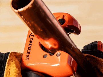 Male plumber using a Crescent pipe cutter to cut copper pipe